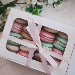 Charming box of assorted macarons wrapped in ribbon, placed with white cherry blossoms on a table.
