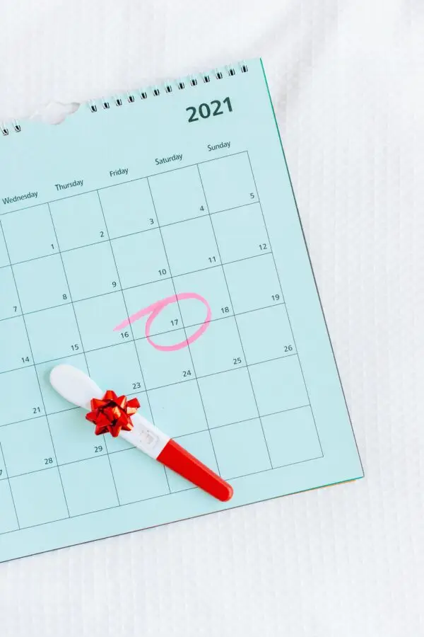 Pregnancy test with ribbon on a calendar, date circled in pink, on white background.